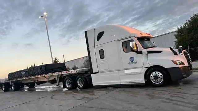 Leading Logistics Inc. Freightliner with a secured flatbed load at sunset